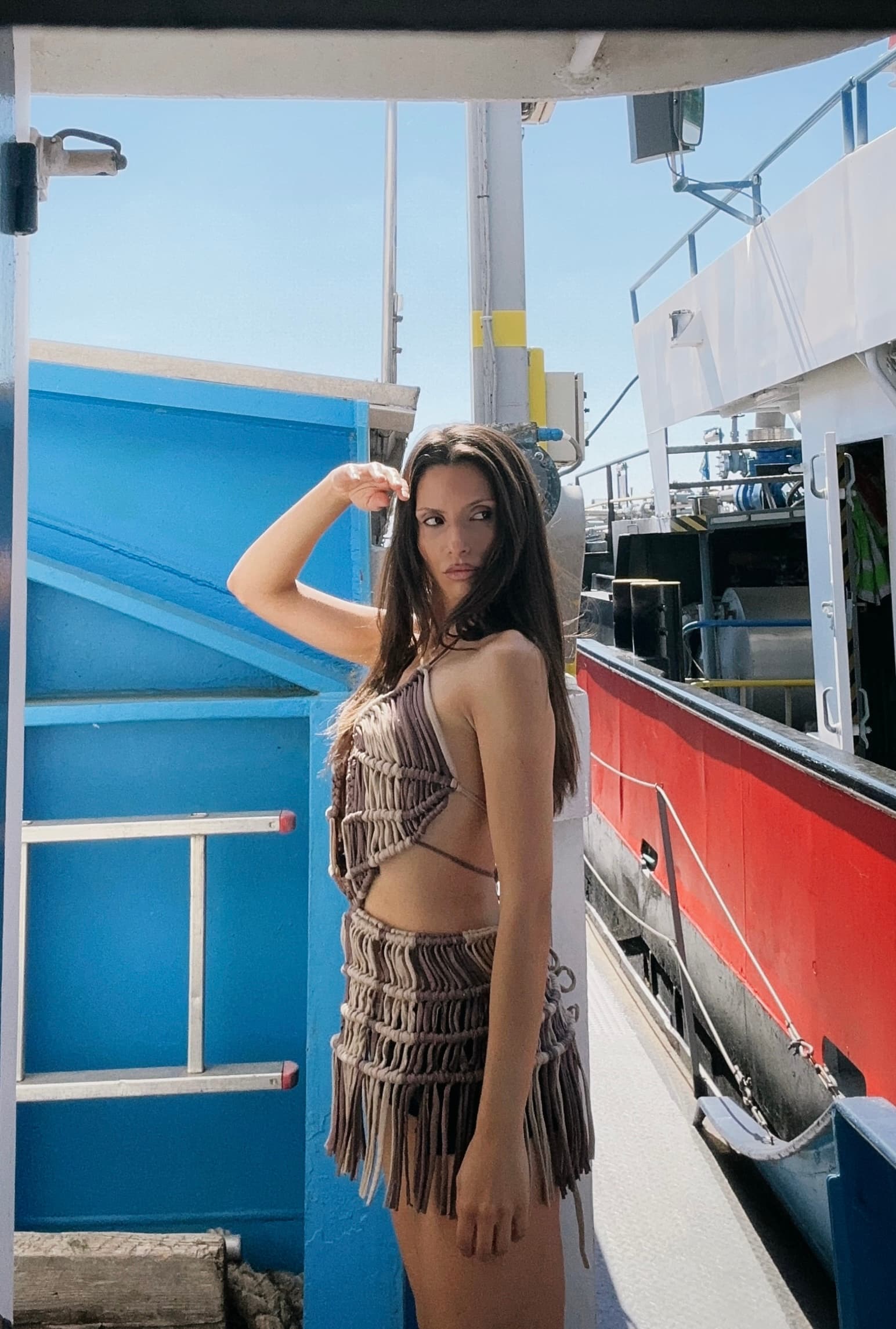 A woman wearing a brown backless fringe mini dress poses on a boat deck.